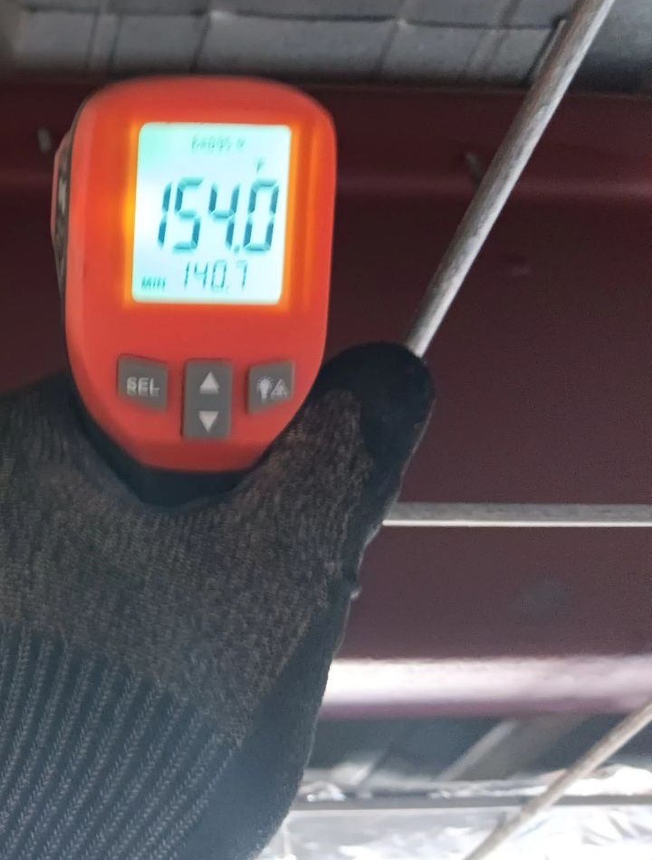 An infrared thermometer reading 154 °F on the underside of a metal roof deck