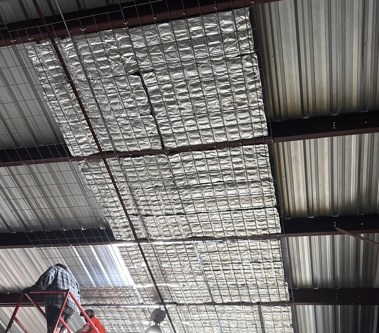Crew installing EnigMAT on wire mesh under a metal roof